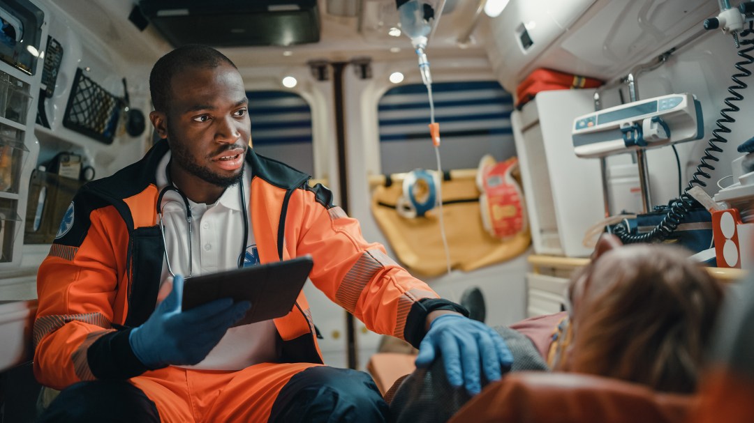A Black EMS Professional Paramedic using a tablet fills in a questionnaire for an injured patient.
